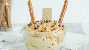 Glass bowl filled with peanut butter dip with pretzels on the side.