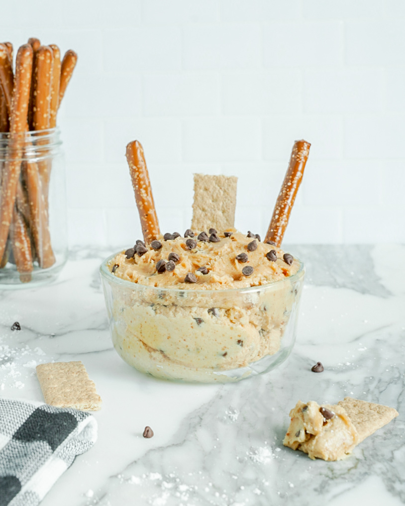 Glass bowl filled with peanut butter dip with pretzels on the side.