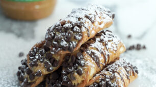 Six peanut butter cannoli's stacked with powdered sugar on top dipped with mini chocolate chips.
