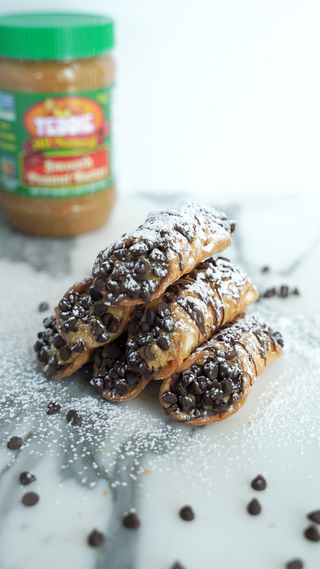 Six peanut butter cannoli's stacked with powdered sugar on top dipped with mini chocolate chips.