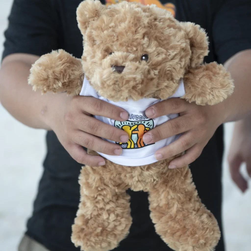 Plush teddy bear wearing a white t-shirt with the Best Buddies logo on it.